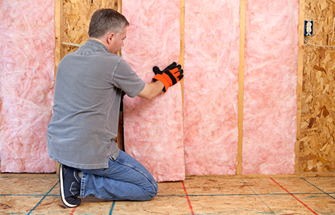 A technician installing fiberglass batt insulation into a wall
