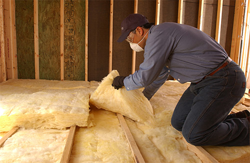 Technician kneeling while installing yellow batt insulation in an attic.