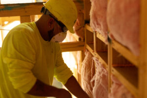 A technician installing fiberglass batt insulation into a wall